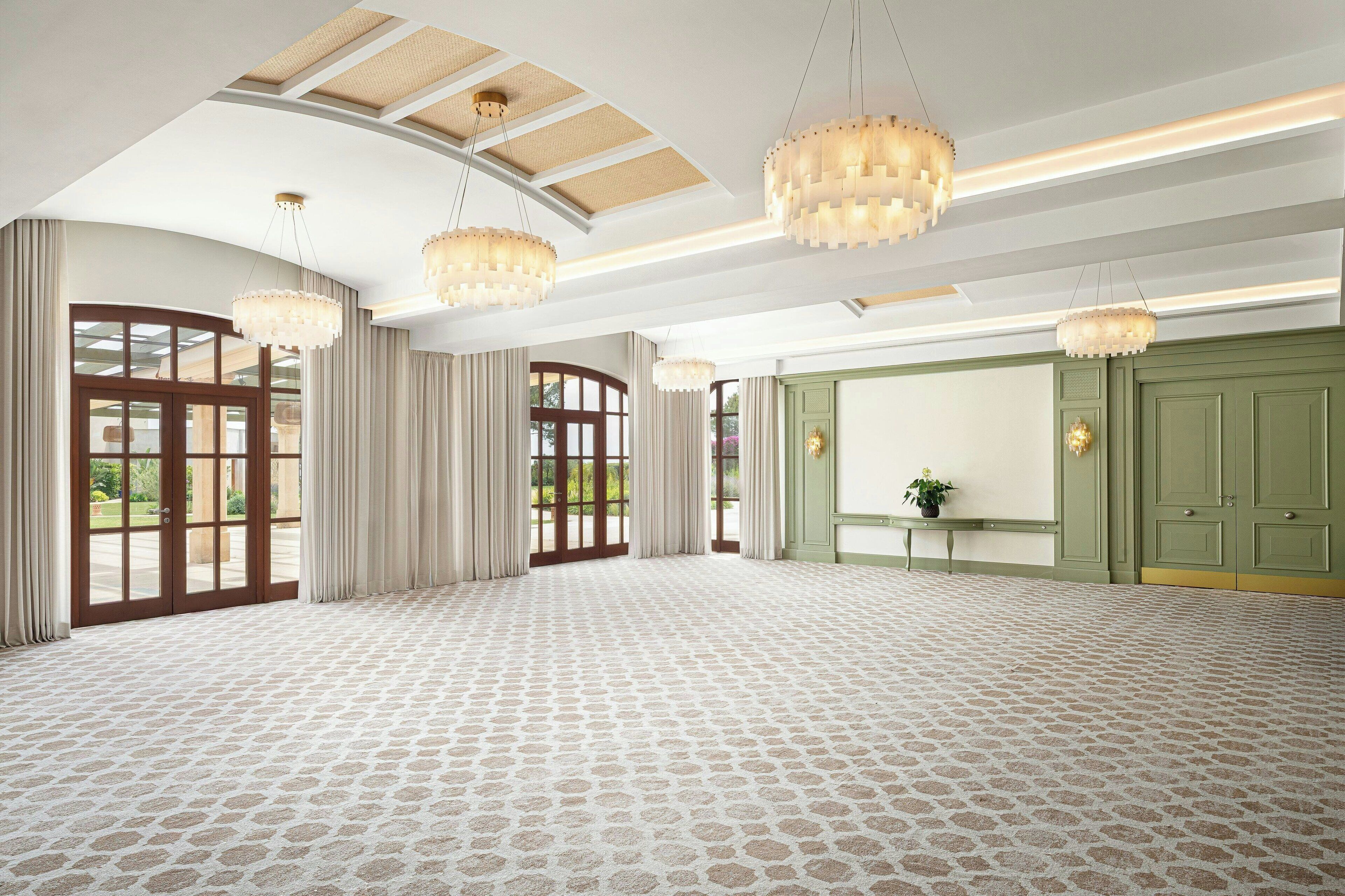 A spacious room with patterned carpet, large windows, and green doors.