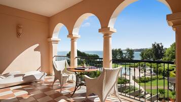 Un balcón con piso a cuadros, muebles de mimbre blanco y vistas a una piscina y zonas verdes.