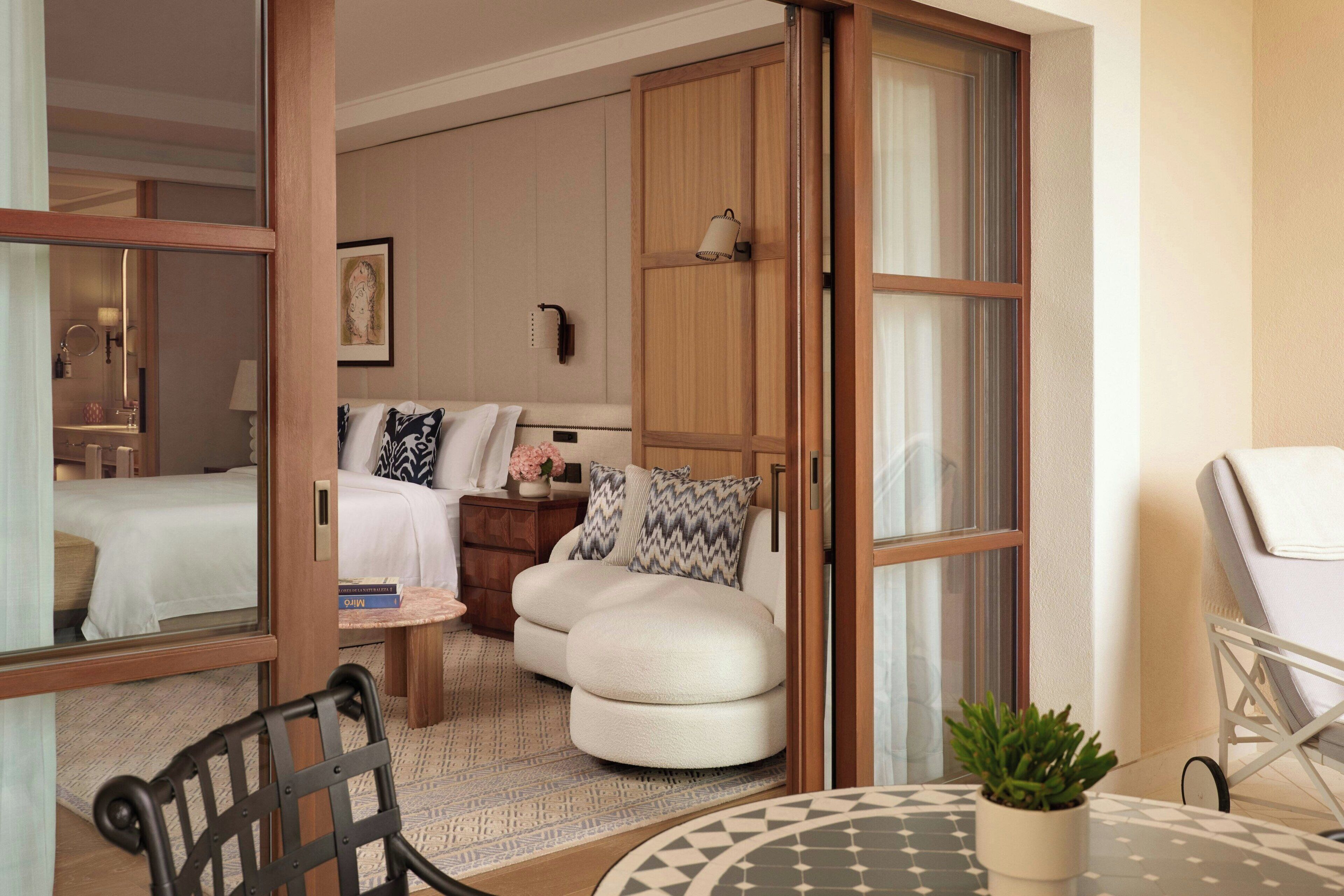 A hotel room with a bed, a seating area with a table, a chair, and a small potted plant.
