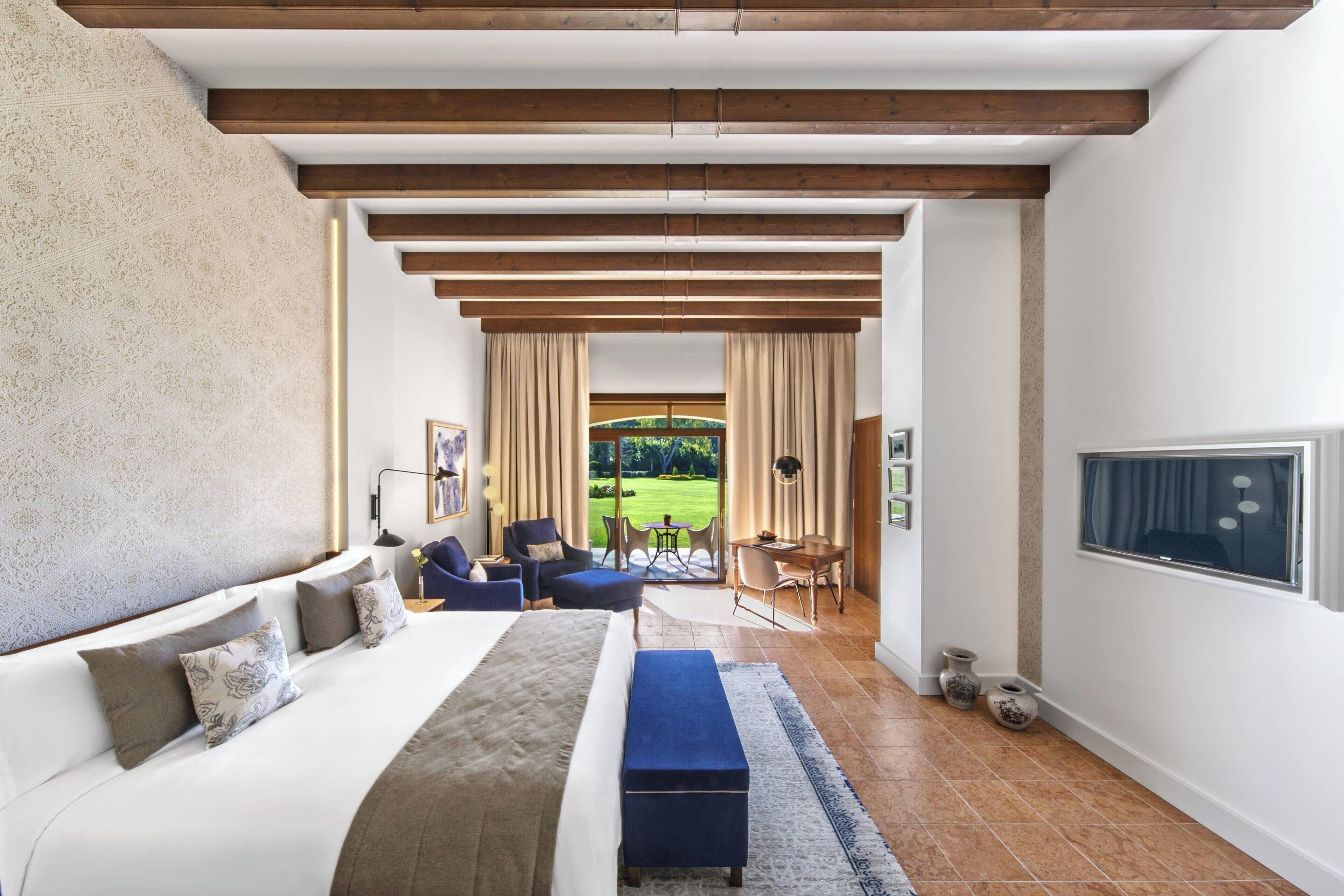 Un dormitorio con una cama grande, un sofá, un escritorio y vistas a un jardín.