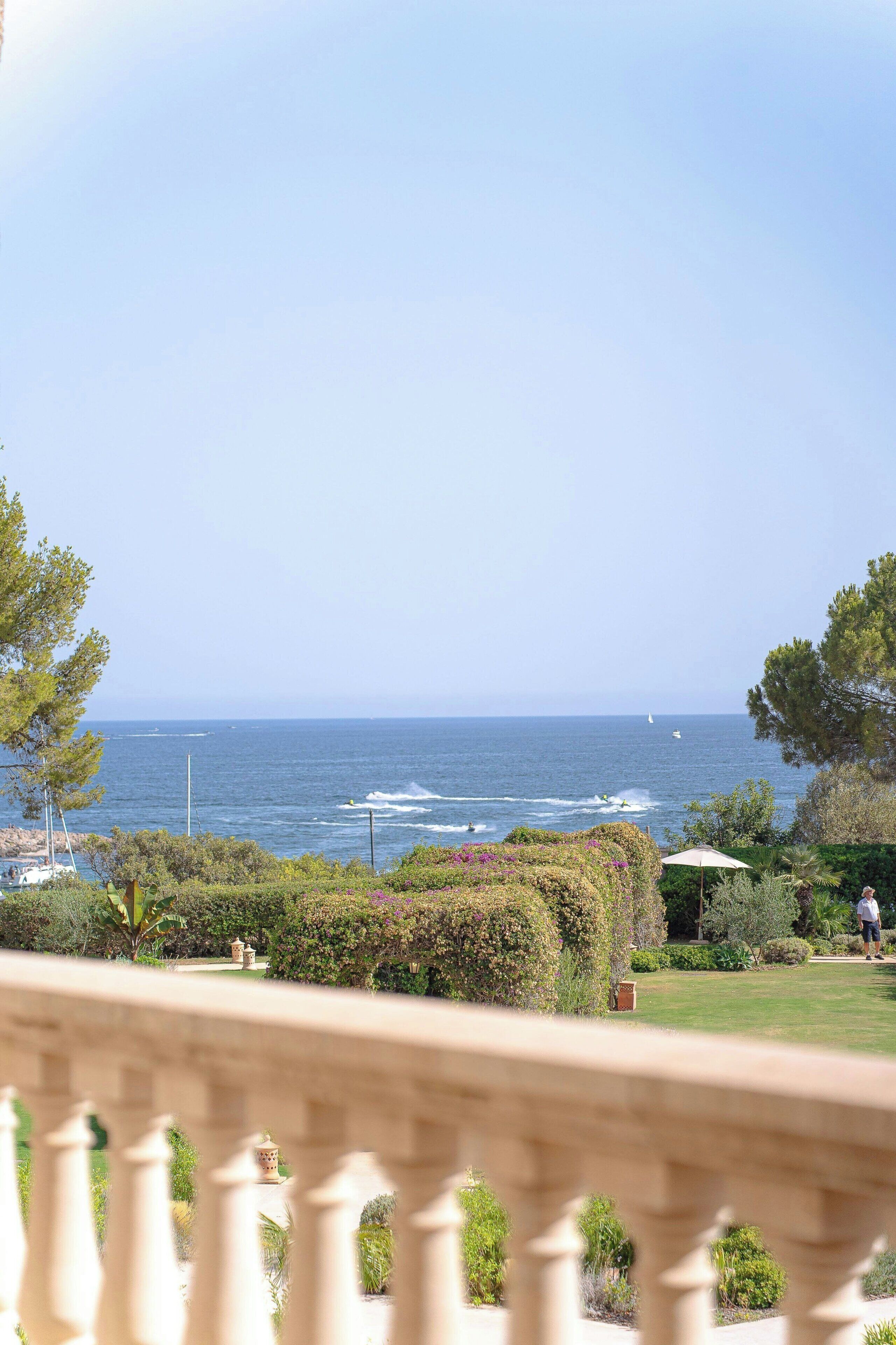 A coastal view from a balcony with a railing, a grassy area, and a clear sky.