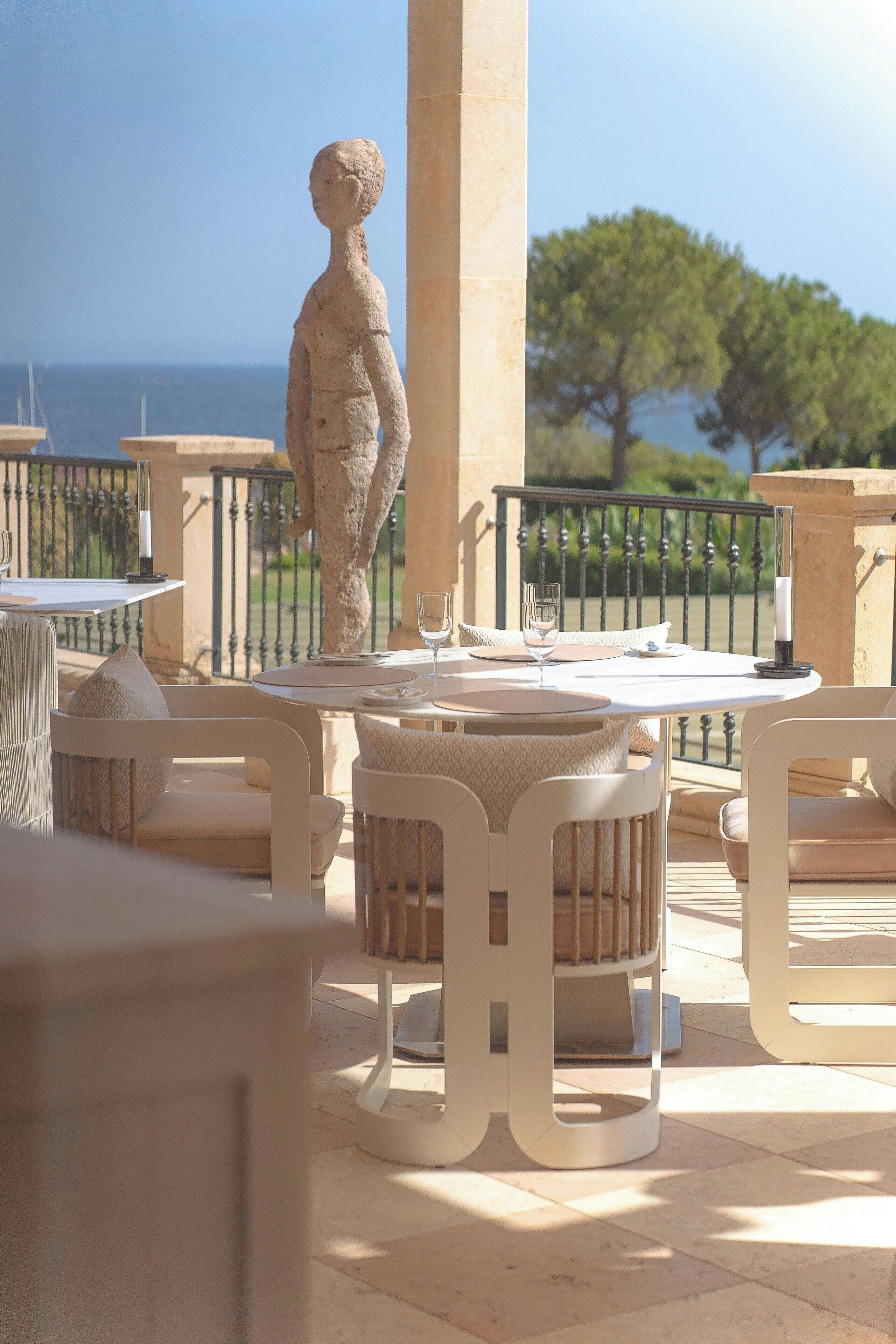 A terrace with white furniture, a stone statue, and a view of the sea.