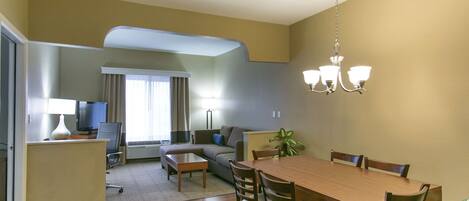 A dining area with a wooden table and chairs, a sofa, a TV, and a plant.