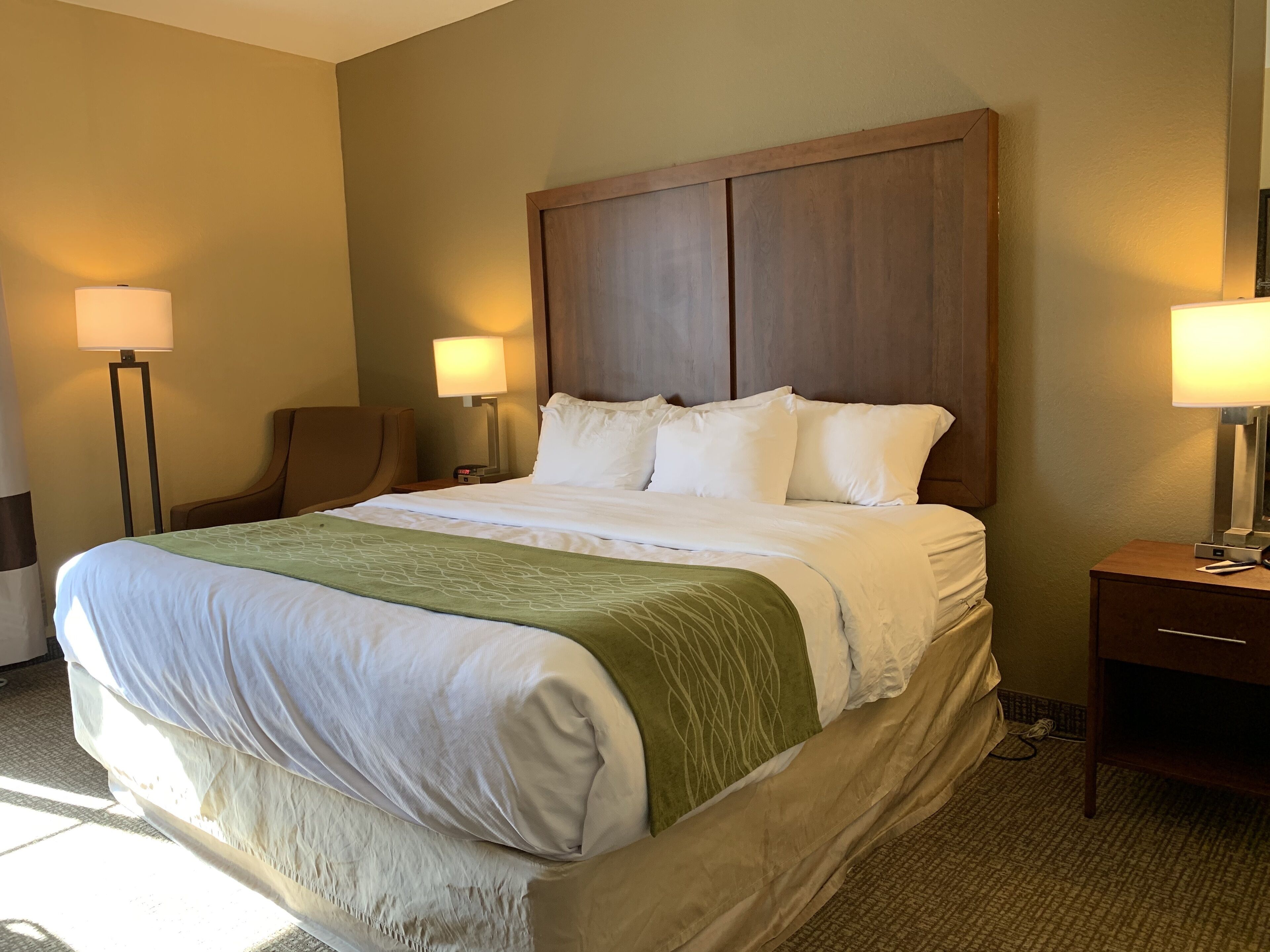 A hotel room with a large bed, two bedside tables with lamps, a chair, and a wooden headboard.