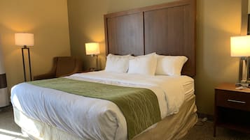 A hotel room with a large bed, two bedside tables with lamps, a chair, and a wooden headboard.