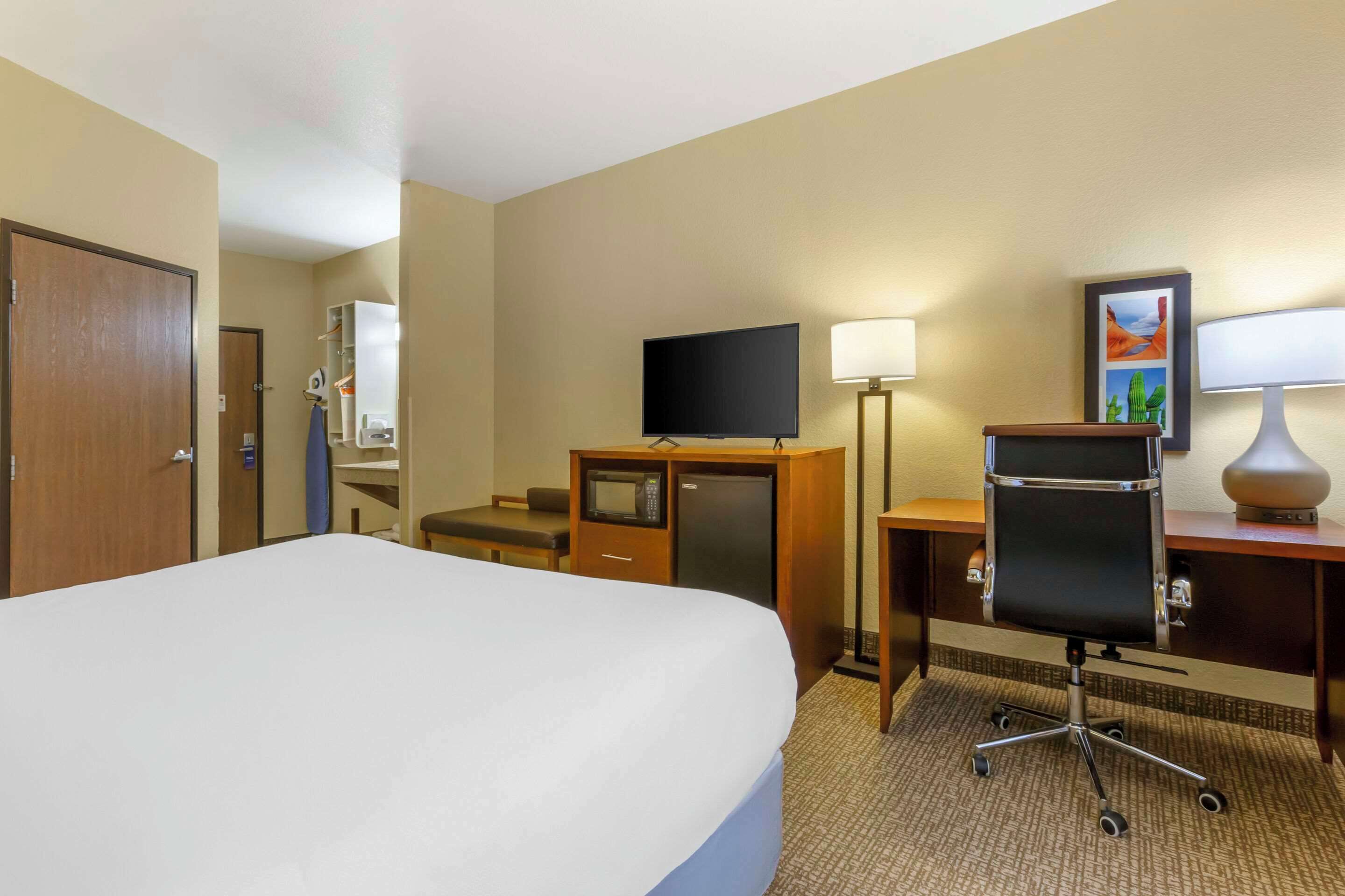 A hotel room with a large bed, a desk with a computer, a television, a desk lamp, and a wall-mounted picture.