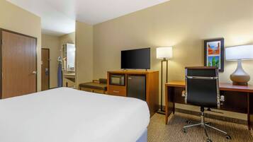 A hotel room with a large bed, a desk with a computer, a television, a desk lamp, and a wall-mounted picture.