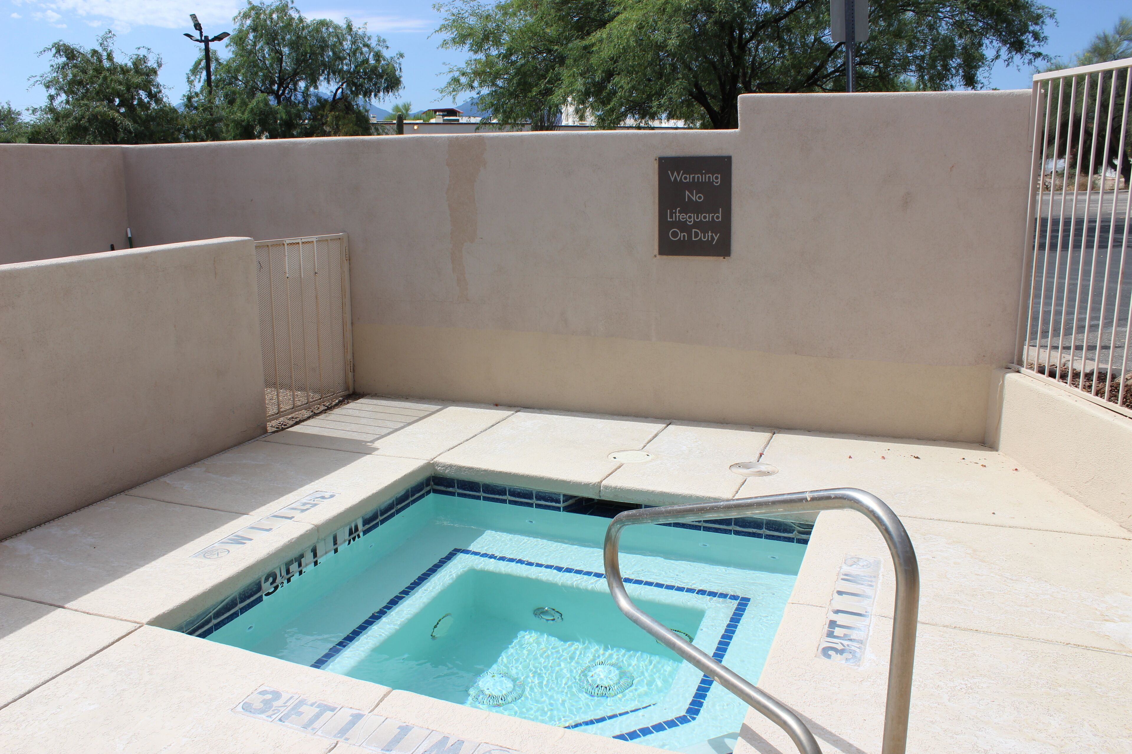 A swimming pool with a lifeguard warning sign, a metal pool ladder, and tiled steps leading into the pool.