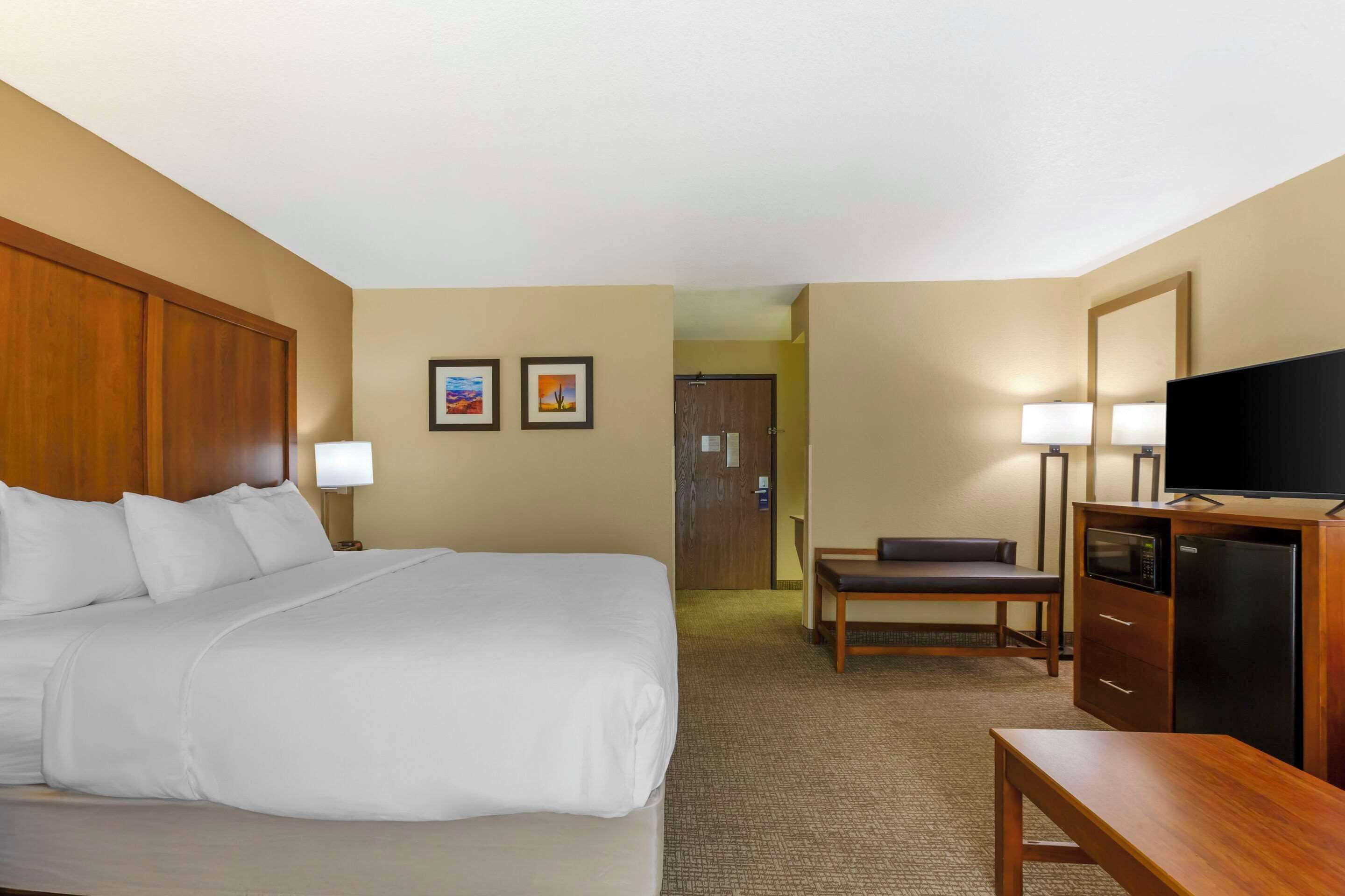 A hotel room with a large bed, a desk, a television, and a door leading to another room.