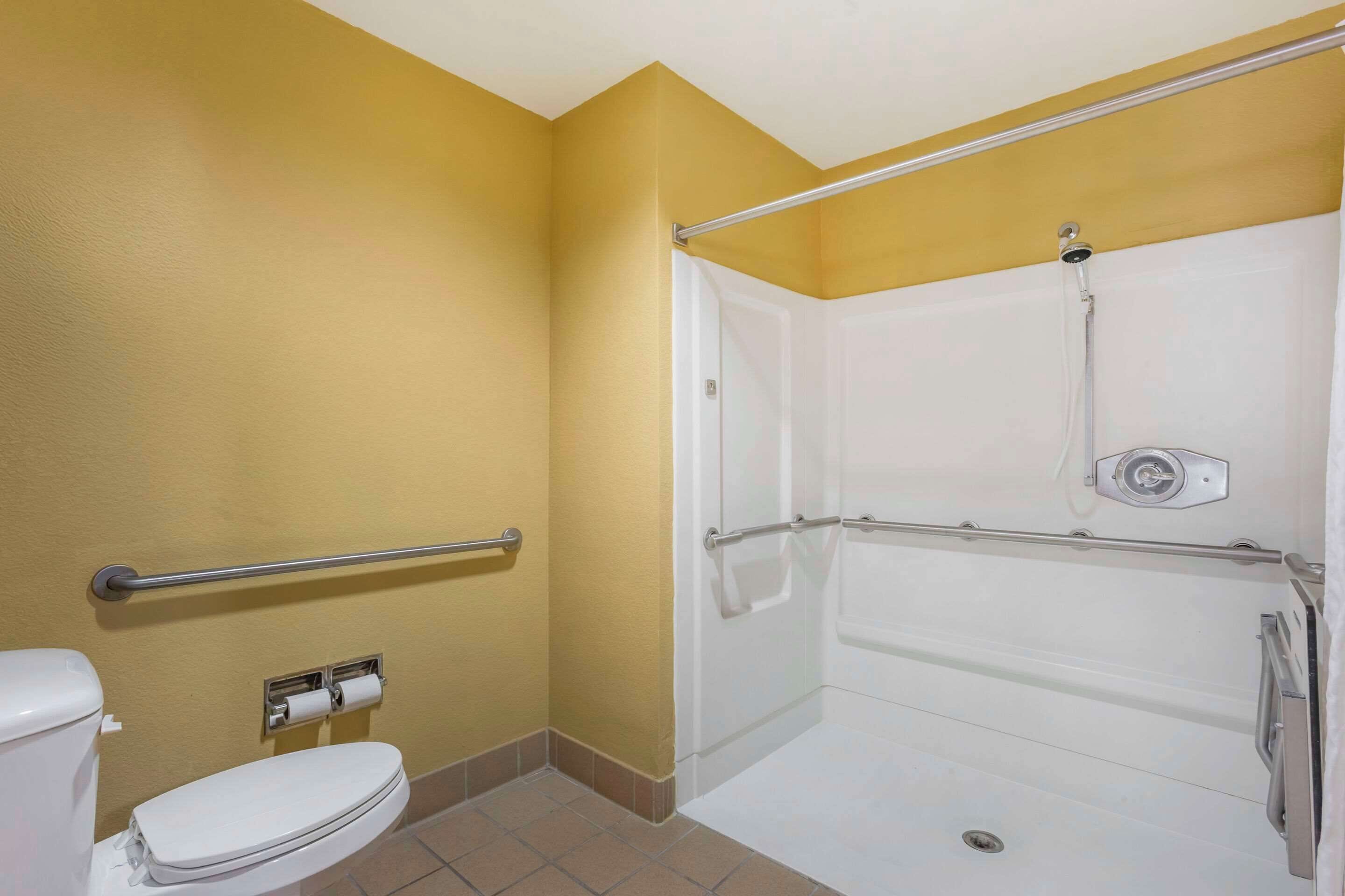 A bathroom with a white toilet, a glass shower enclosure, and a handrail.