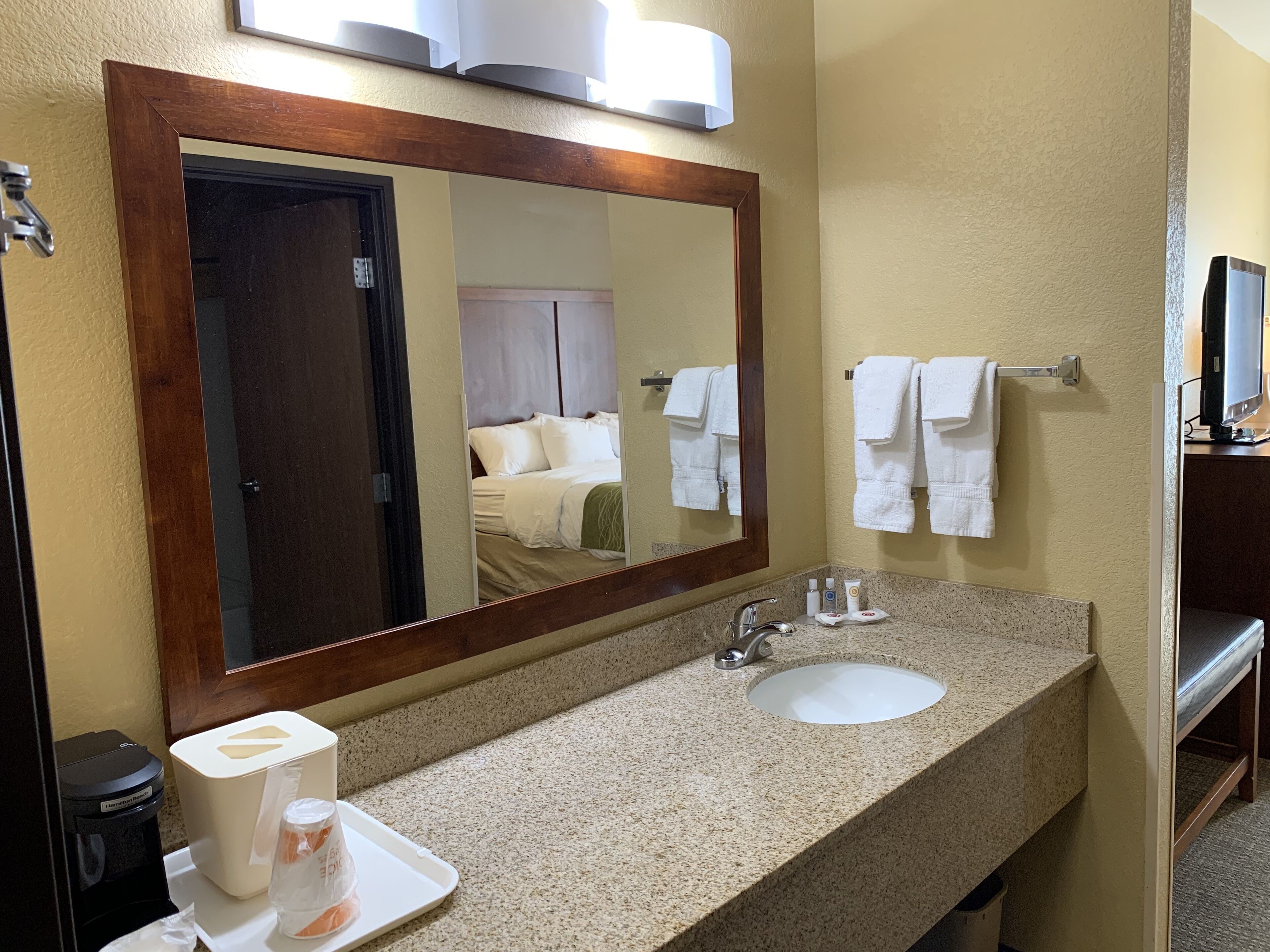 A hotel bathroom with a large mirror, a sink, and a towel rack.