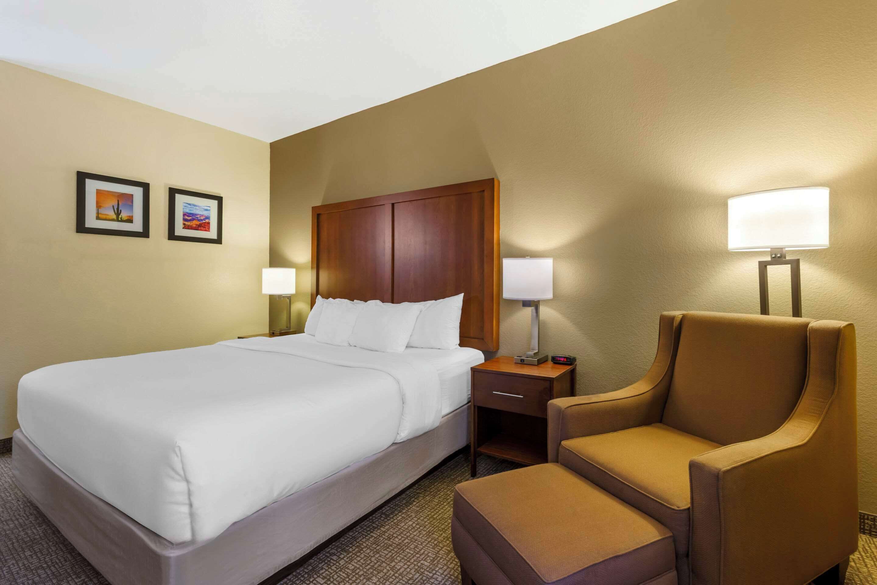 A hotel room with a large bed, two bedside tables with lamps, a wooden headboard, and two framed pictures on the wall.