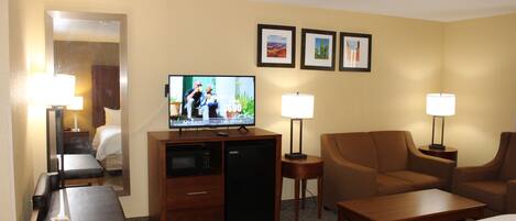 Ein Hotelzimmer mit einem Bett, einem Schreibtisch mit Computer, einem Fernseher, einer Couch und zwei Lampen.