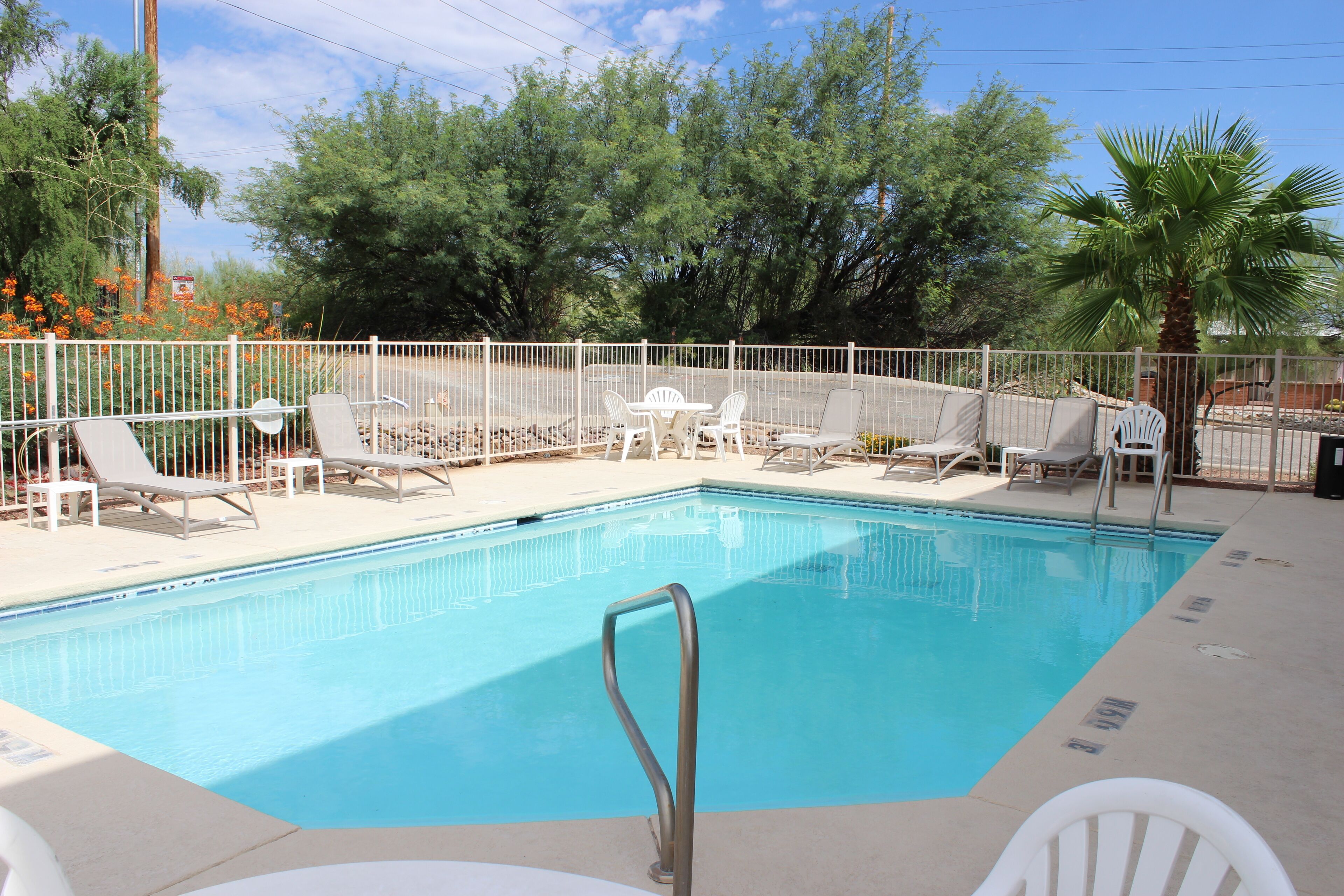 Una piscina rectangular con una escalera metálica, rodeada de sillas de descanso blancas y una cerca también blanca.