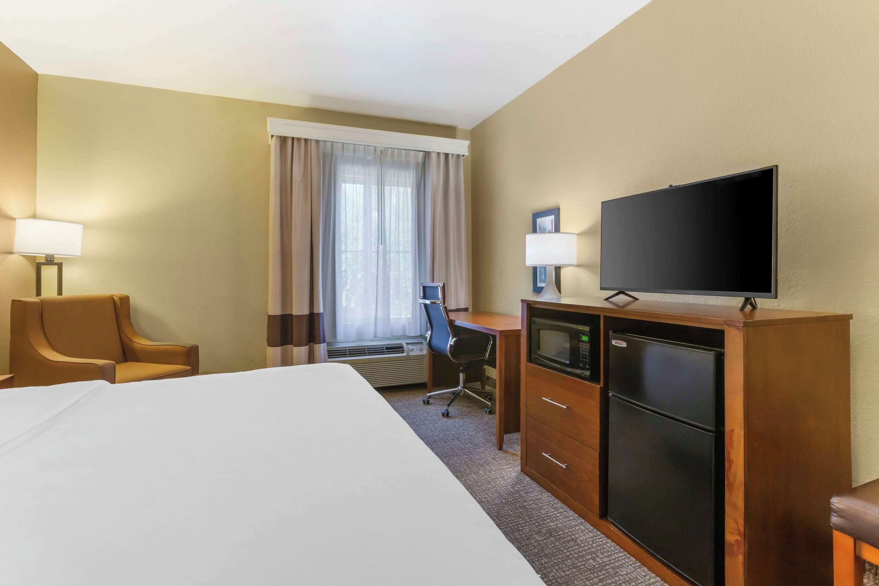 Habitación de hotel con una cama grande, un escritorio con computadora, televisor y minibar.