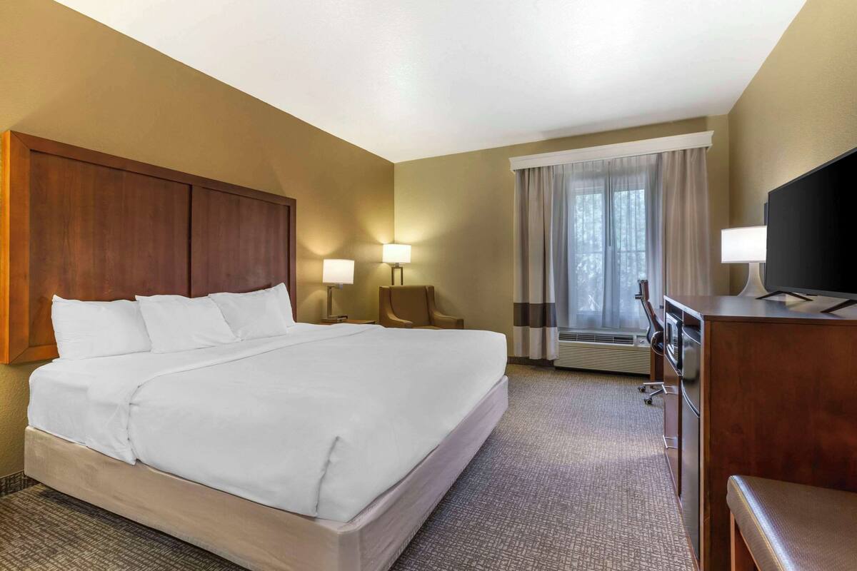 Ein Hotelzimmer mit einem großen Bett, zwei Nachttischlampen, einem Schreibtisch mit Fernseher und einem Fenster mit Vorhängen.