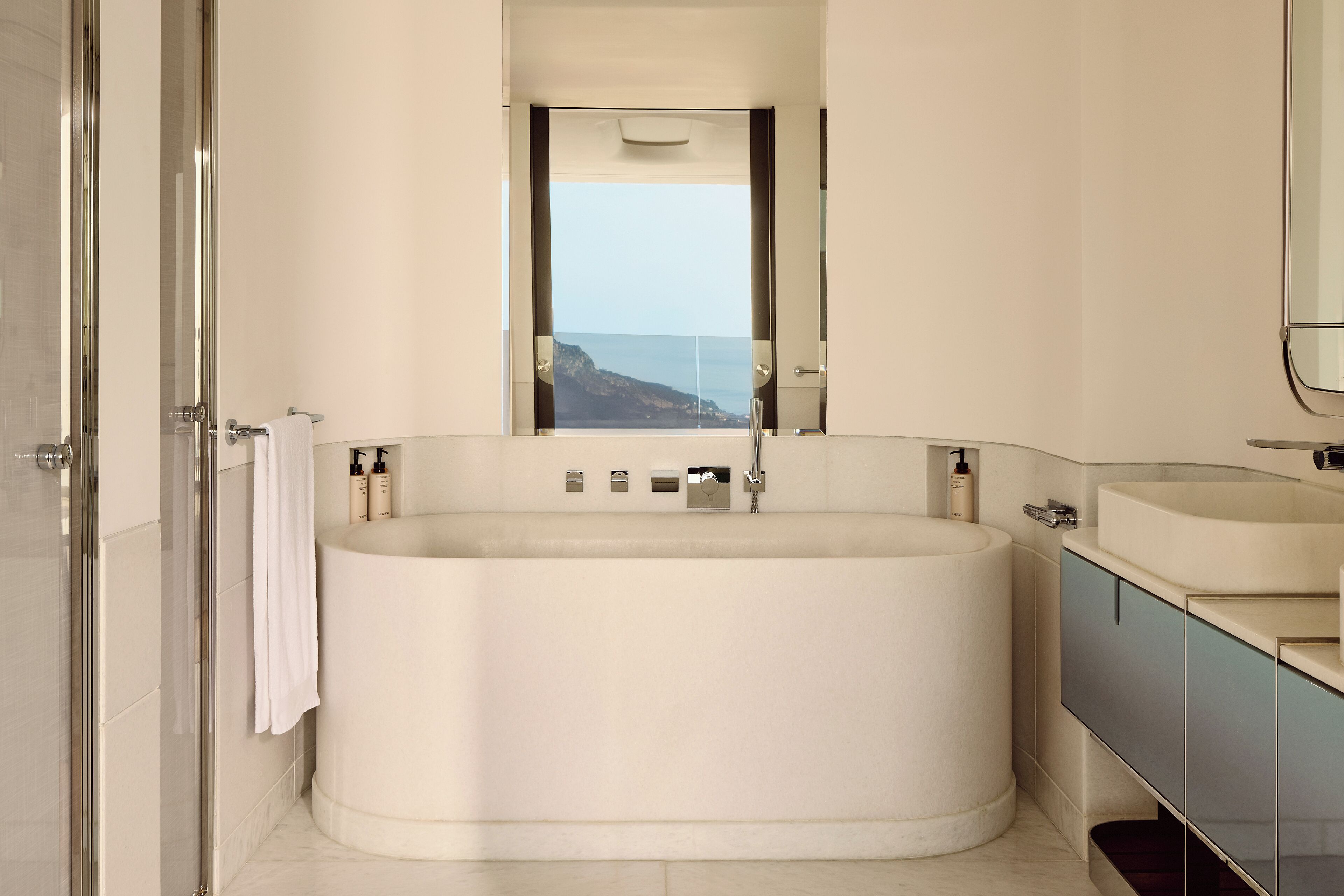 A modern bathroom with a large bathtub, a glass shower enclosure, and a view of the ocean.