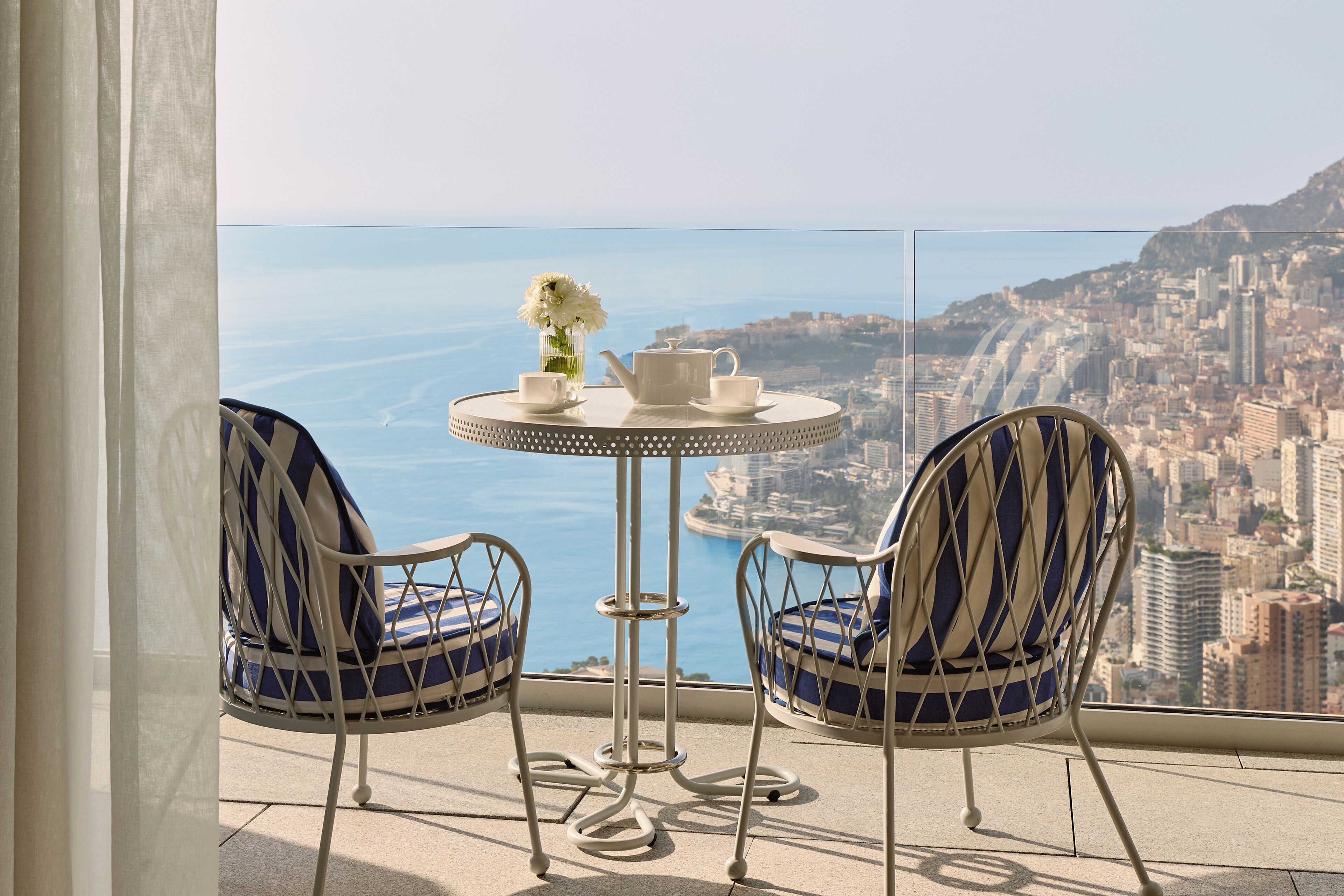 Een balkon met een tafel, twee stoelen en uitzicht op een stad en zee.