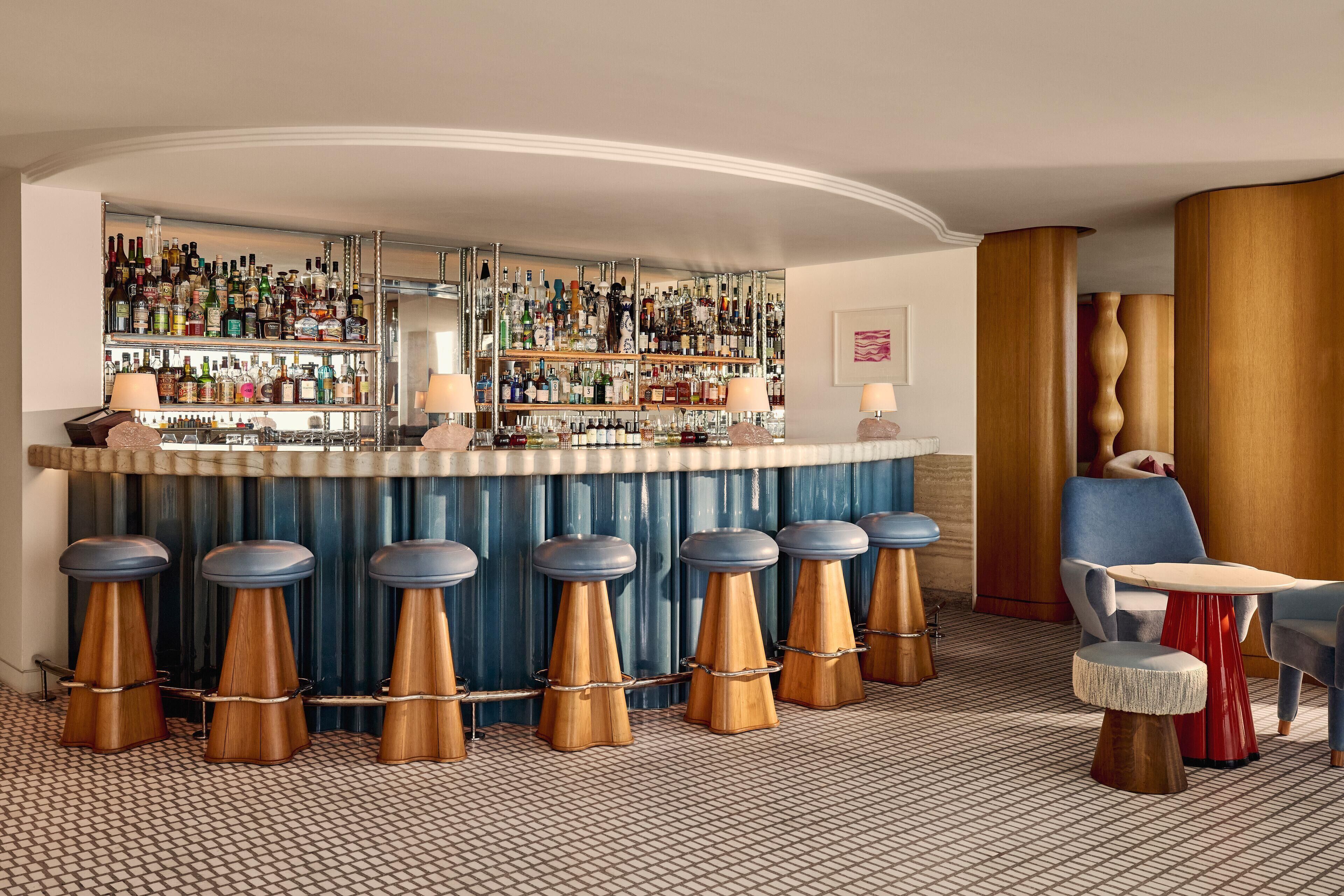 A bar area with stools, a bar counter, and a variety of bottles.