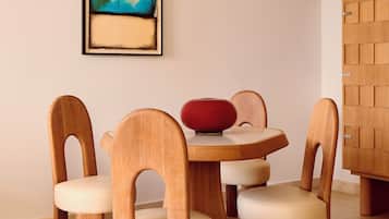 Un comedor con una mesa redonda de madera, cuatro sillas de madera con asientos acolchados y un florero rojo sobre la mesa.
