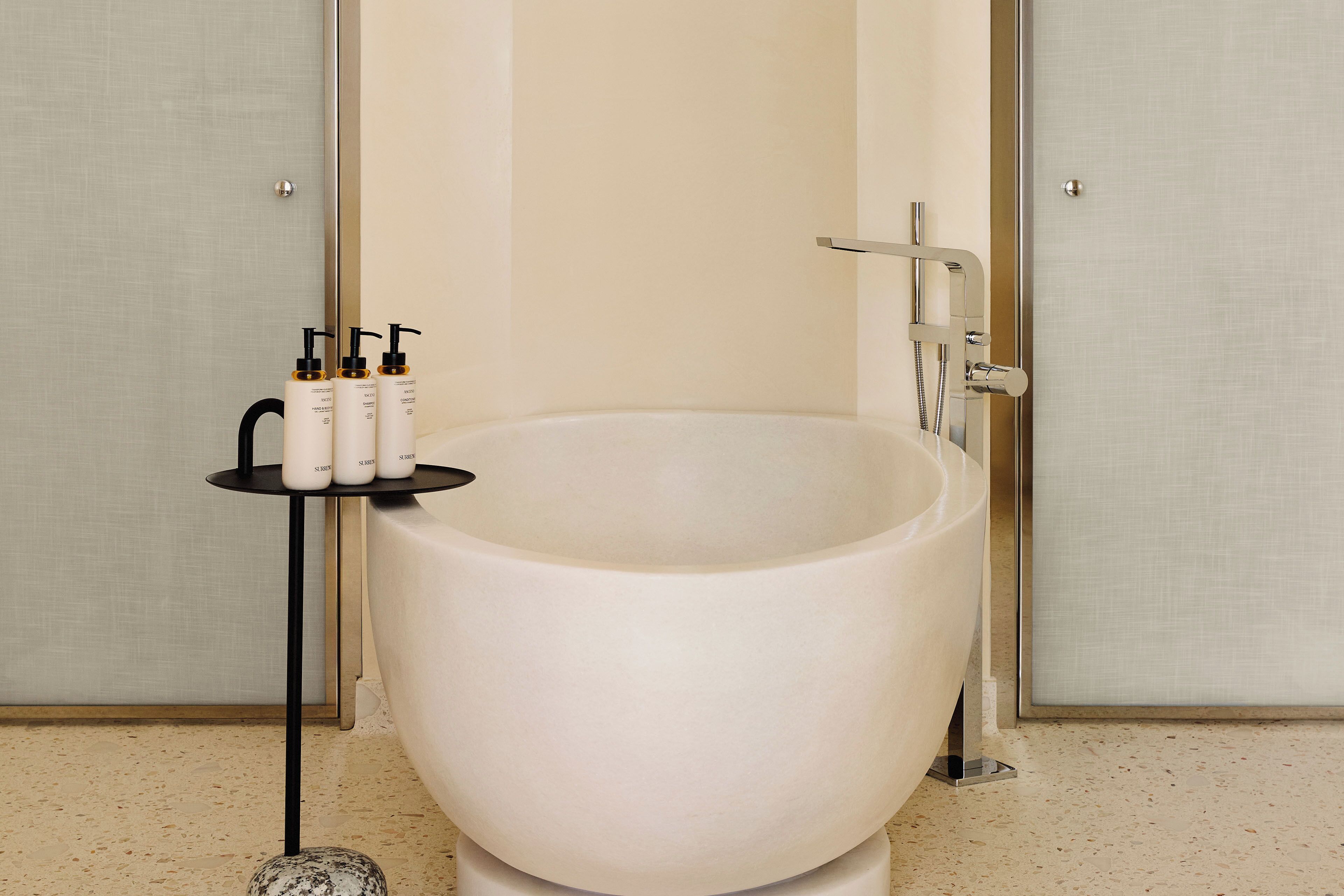 A large bathtub with a modern faucet, a small shelf with toiletries, and a textured wall.