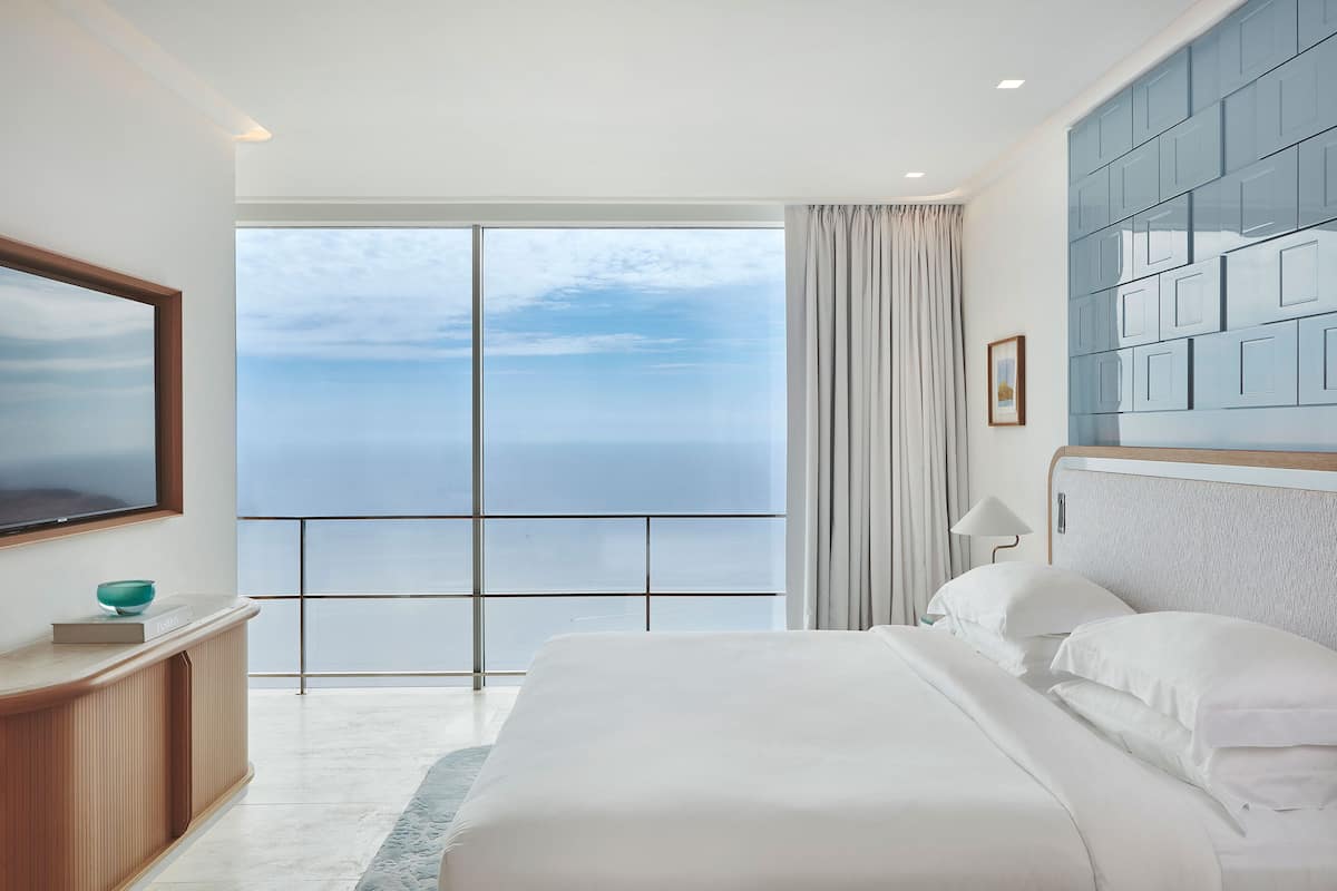 A bedroom with a large bed, a TV, a view of the ocean, and a modern design.