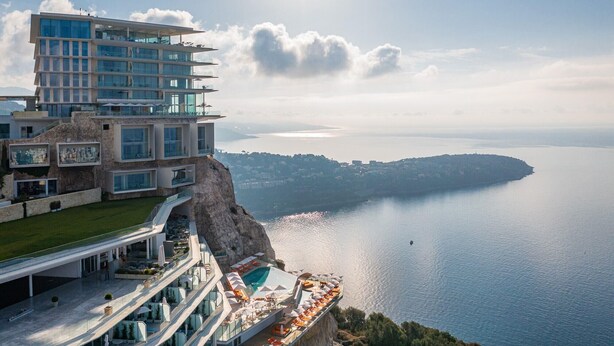 Un hotel a più piani con piscina e area salotto all'aperto che si affaccia su un corso d'acqua.