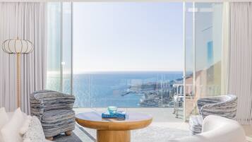 A modern living room with a large window, two armchairs, a round wooden coffee table, and a view of the sea.