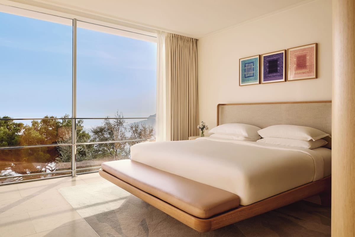 A modern bedroom with a large bed, a view of the outdoors, and three framed pictures on the wall.
