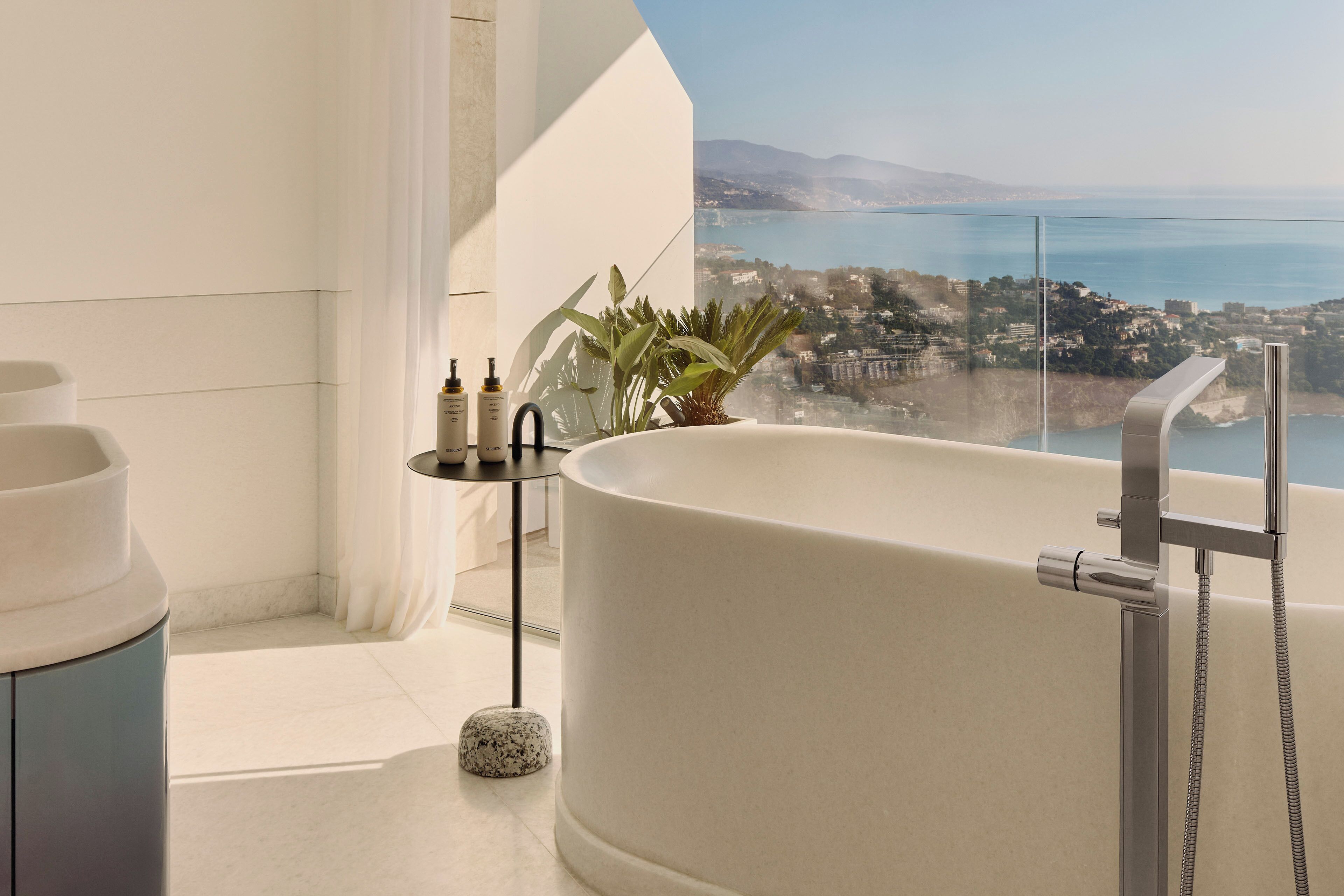 A modern bathroom with a freestanding bathtub, a glass shower enclosure, and a view of a coastal city.