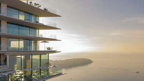 Un edificio moderno con numerosi balconi affacciato su un mare tranquillo e un'isola in lontananza.