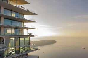Un edificio moderno con numerosi balconi affacciato su un mare tranquillo e un'isola in lontananza.