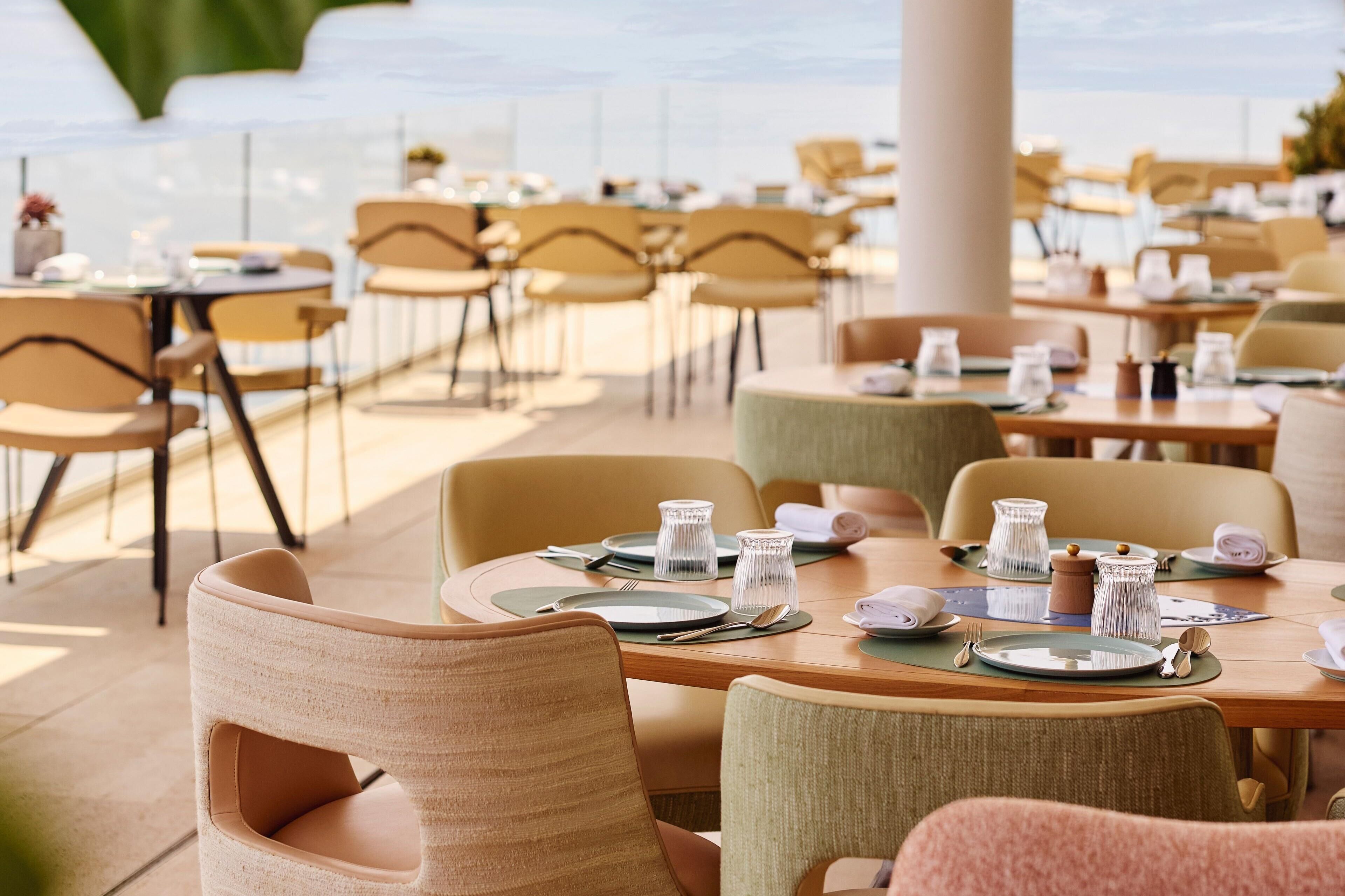 Un restaurant avec des tables dressées, des chaises et une vue sur la mer.