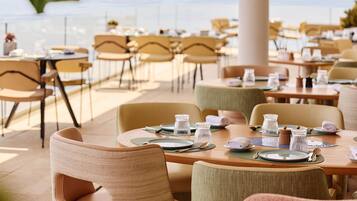 Un restaurant avec des tables dressées, des chaises et une vue sur la mer.