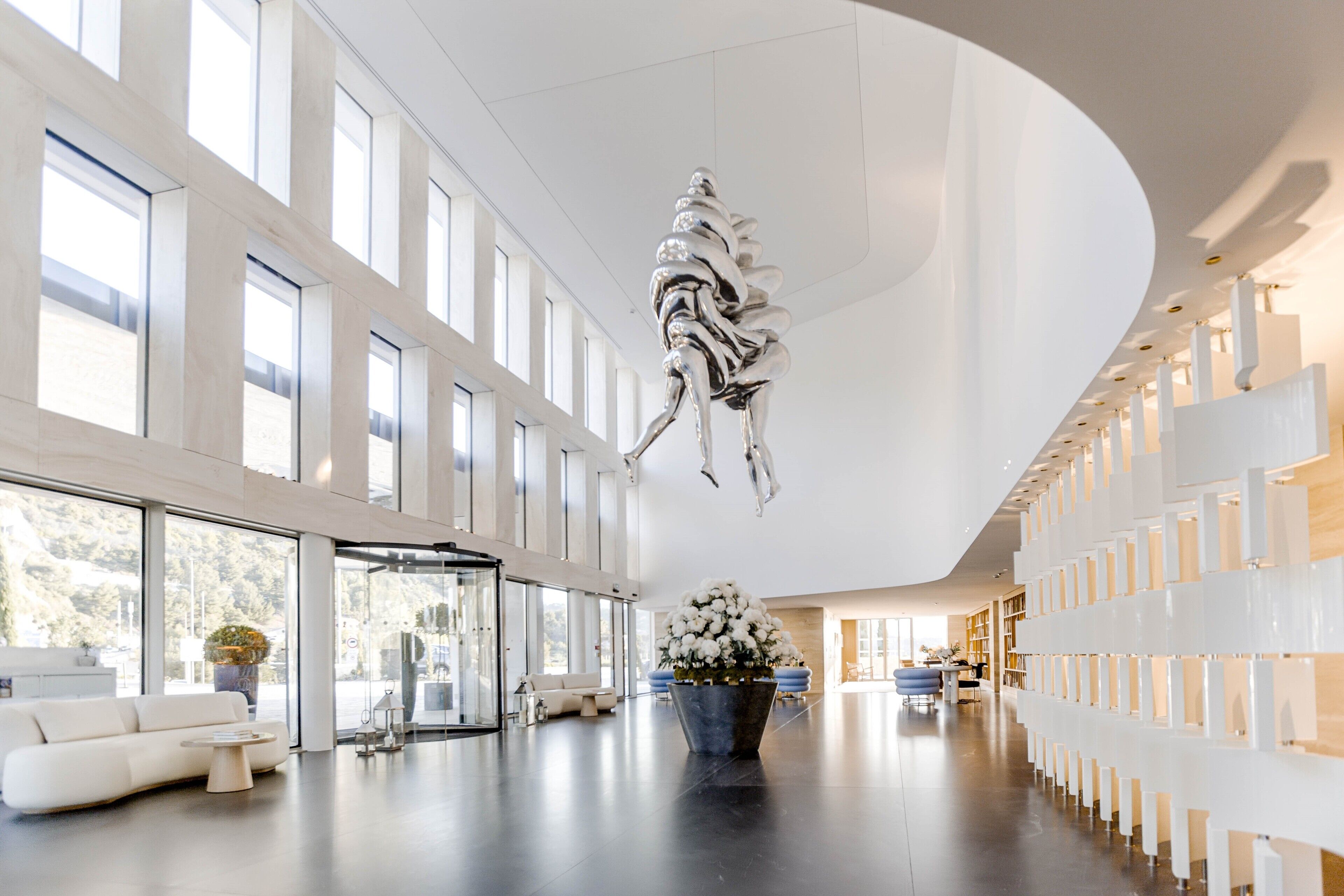 A spacious lobby with a modern design, featuring a large sculpture, a white sofa, and a potted plant.