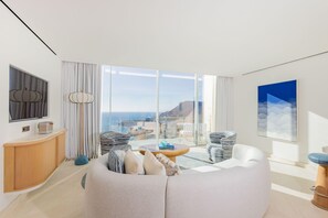 A modern living room with a sofa, a round coffee table, and a view of the ocean through large windows. - The Maybourne Riviera, Maybourne  (Roquebrune-Cap-Martin)