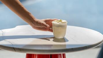 A hand holding a glass of white beverage on a white table with a red base.