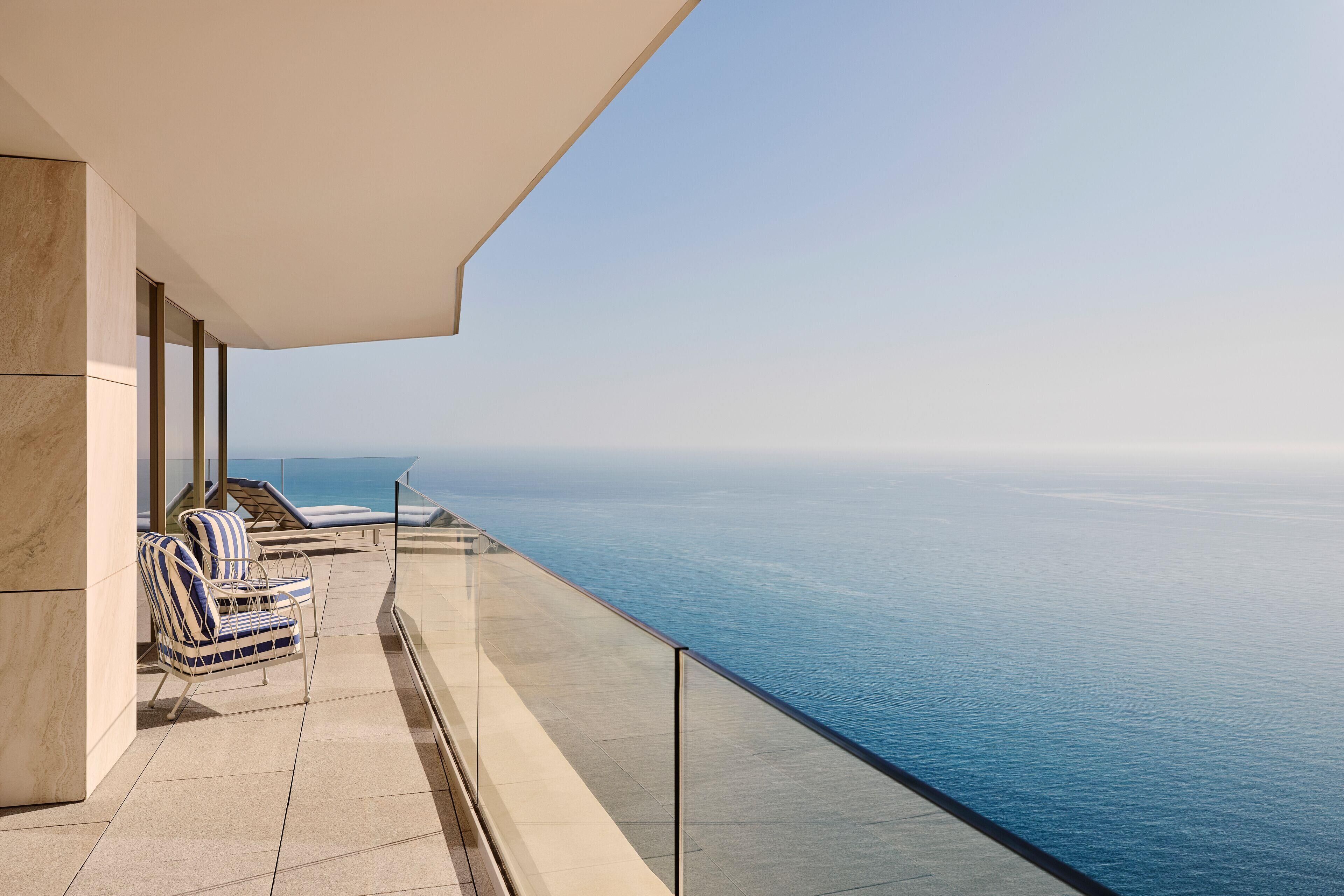 A balcony with a view of the ocean, a lounge chair, and a glass railing.