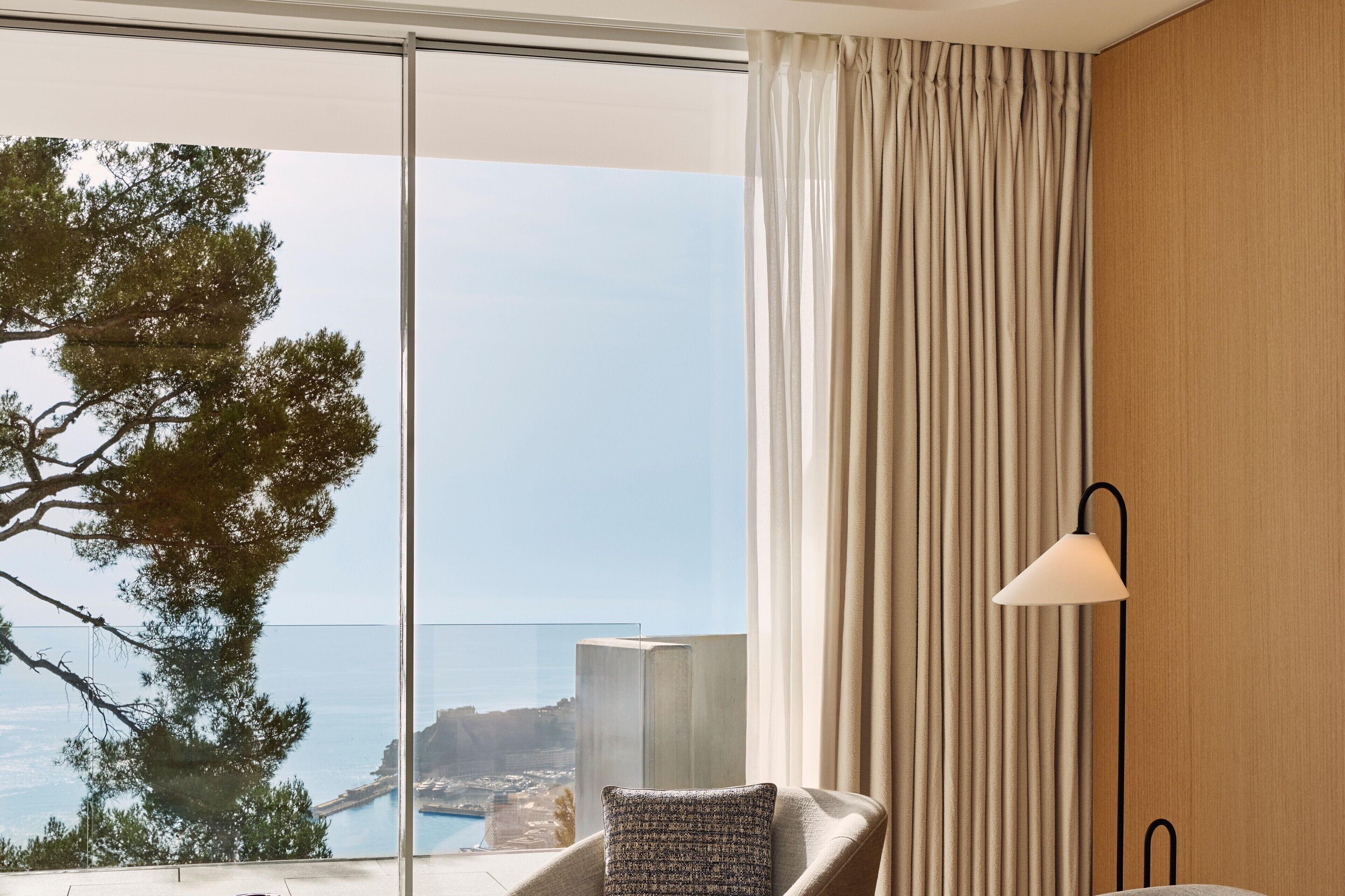 Una habitación con vista al mar, una silla con un cojín estampado y una lámpara.