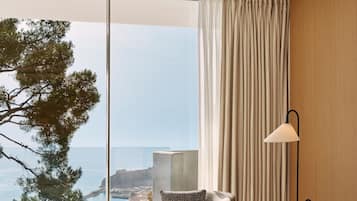 Una habitación con vista al mar, una silla con un cojín estampado y una lámpara.