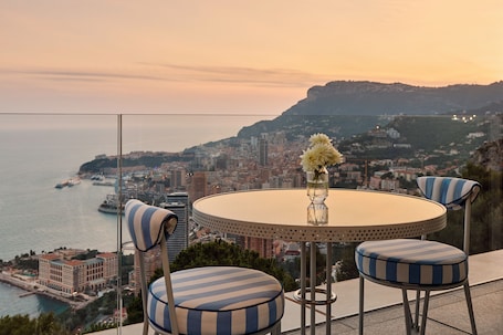 A round table with a vase of flowers, two striped chairs, and a city view.