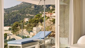 Un balcone con una poltrona prendisole, un tavolo e un ombrellone.