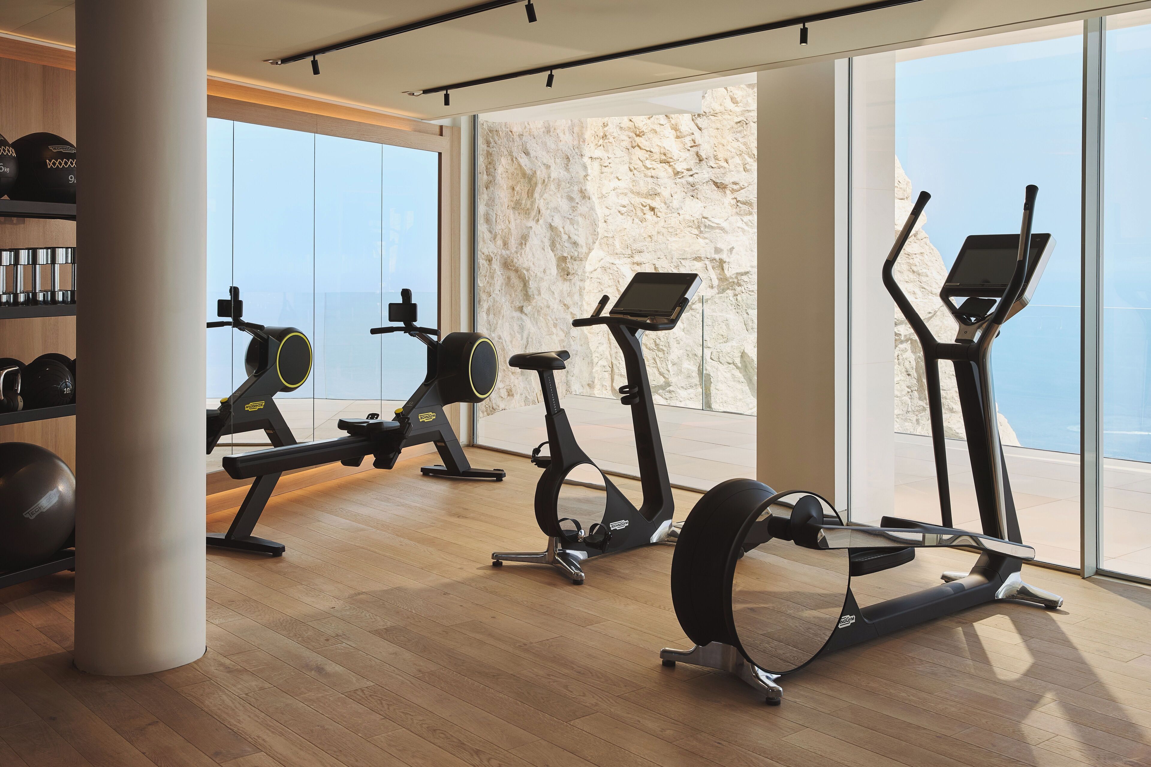 A gym with cardio machines, weight equipment, and large windows offering a view of the outdoors.