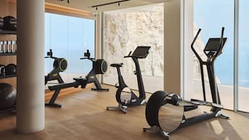 A gym with cardio machines, weight equipment, and large windows offering a view of the outdoors.