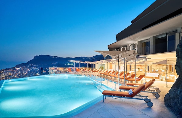 Una piscina al aire libre, sombrillas, sillones reclinables de piscina