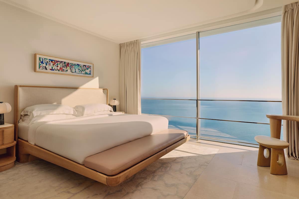 A modern hotel room with a large bed, a view of the sea, and a painting on the wall.