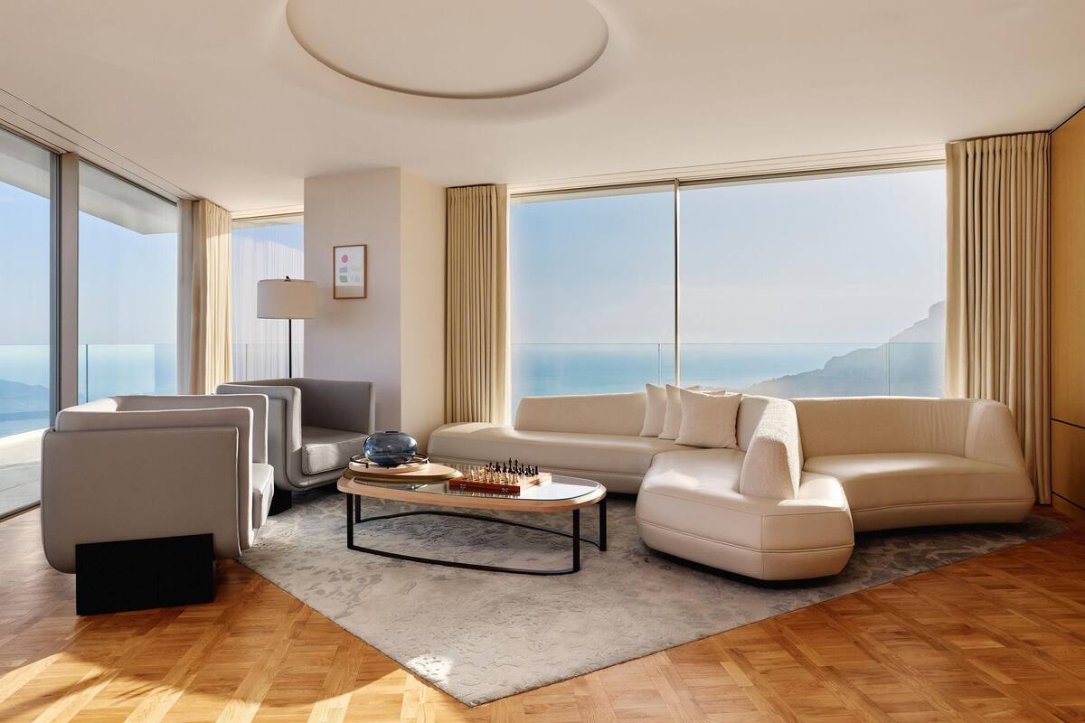 A modern living room with a large window, a sofa, a coffee table, and a lamp.