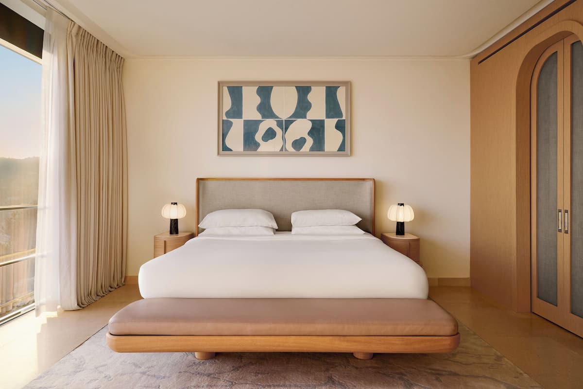 A modern bedroom with a large bed, two bedside tables with lamps, a large abstract painting, and a wardrobe.