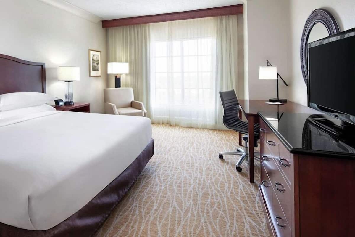 Une chambre d’hôtel avec un grand lit, un bureau avec une chaise, une télévision et une fenêtre avec des rideaux.