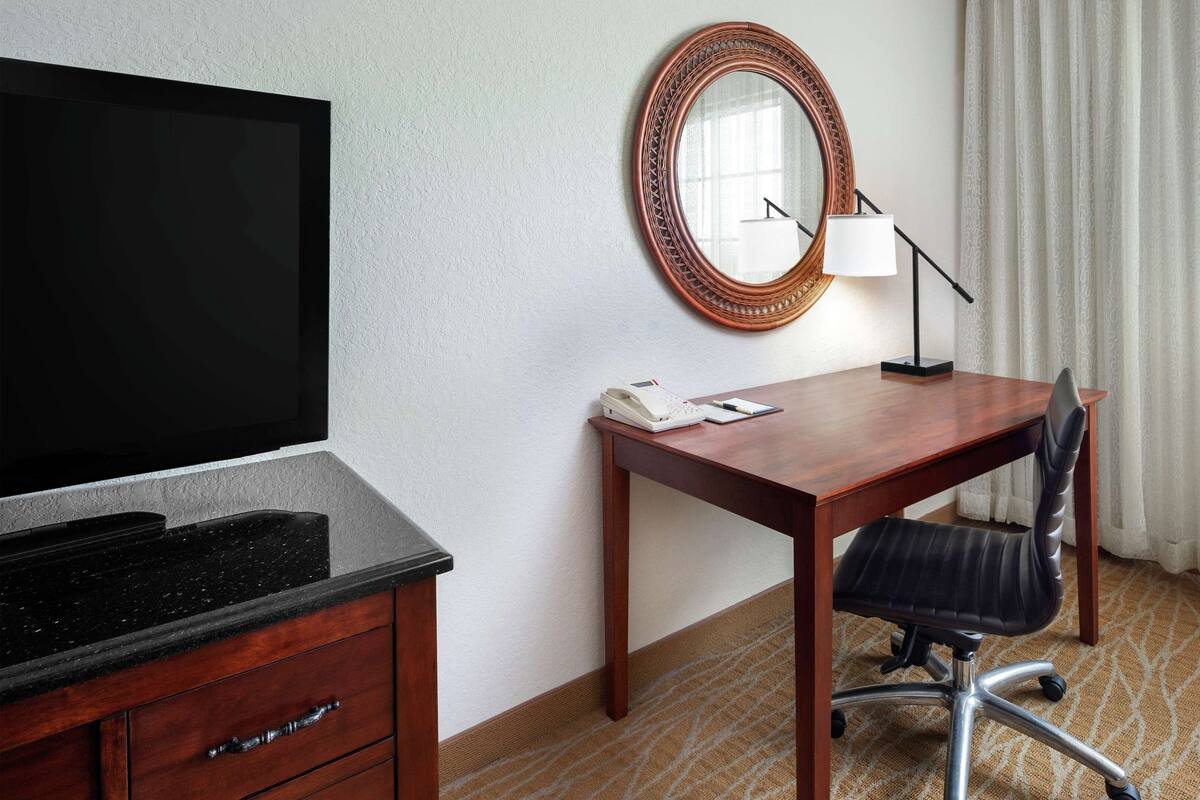 Une chambre d’hôtel avec un bureau en bois, un fauteuil en cuir noir, une télévision, un téléphone et une lampe.